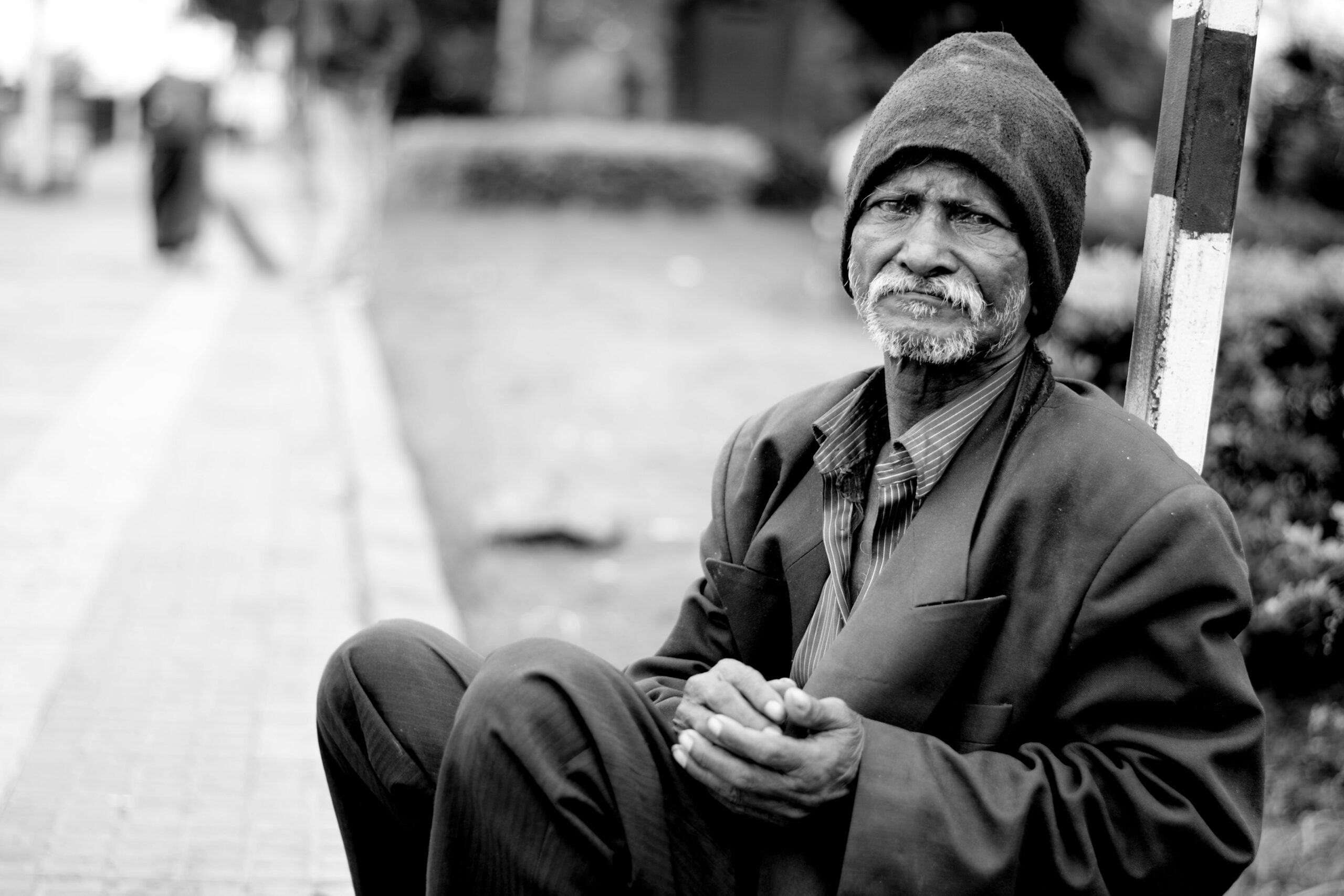 Homeless man sitting on sidewalk looking for assistance.